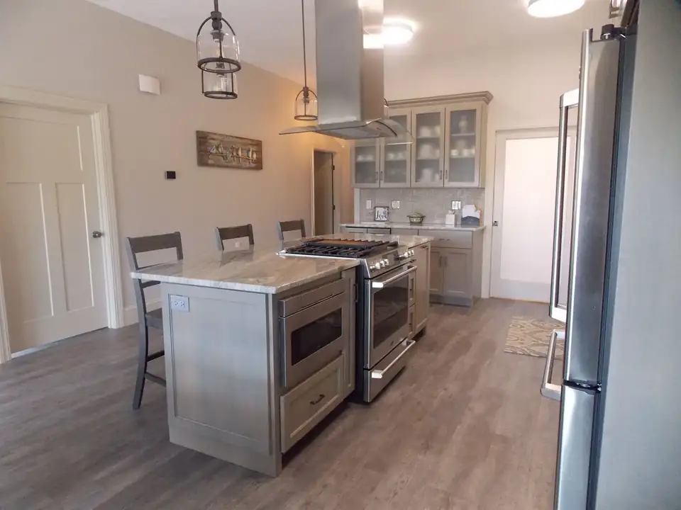 Kitchen cabinets in Uxbridge: gray painted kitchen with a stone-topped island, glass-front uppers, stainless range hood and pendant lights