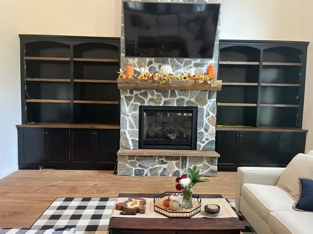 Black built-in bookcases and lower cabinets on both sides of a stone fireplace in a living room