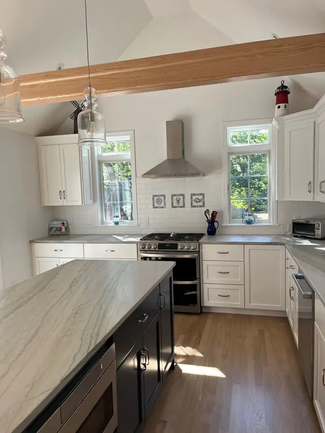 White painted shaker cabinets, dark island with a white and gray stone top, stainless hood and vaulted ceiling with a wood beam