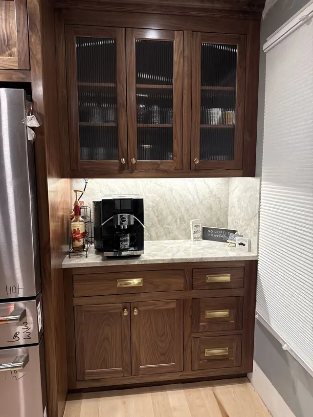 Dark wood coffee bar cabinet with glass-front uppers, brass pulls and a stone backsplash